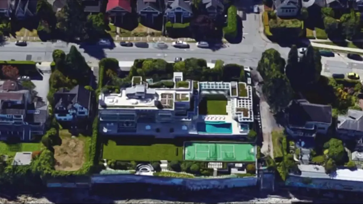 Aerial view of a flat-roofed modern waterfront mansion with a swimming pool and tennis court among Vancouver streets