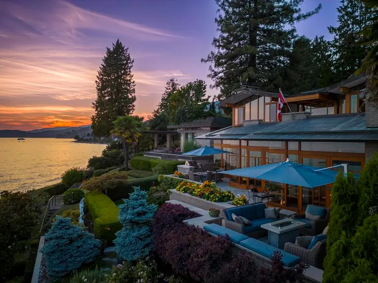 A terraced hillside house above the water at sunset, with landscaped gardens and patio seating