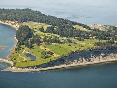 An aerial view of a wooded private island with a golf course running down to the shoreline