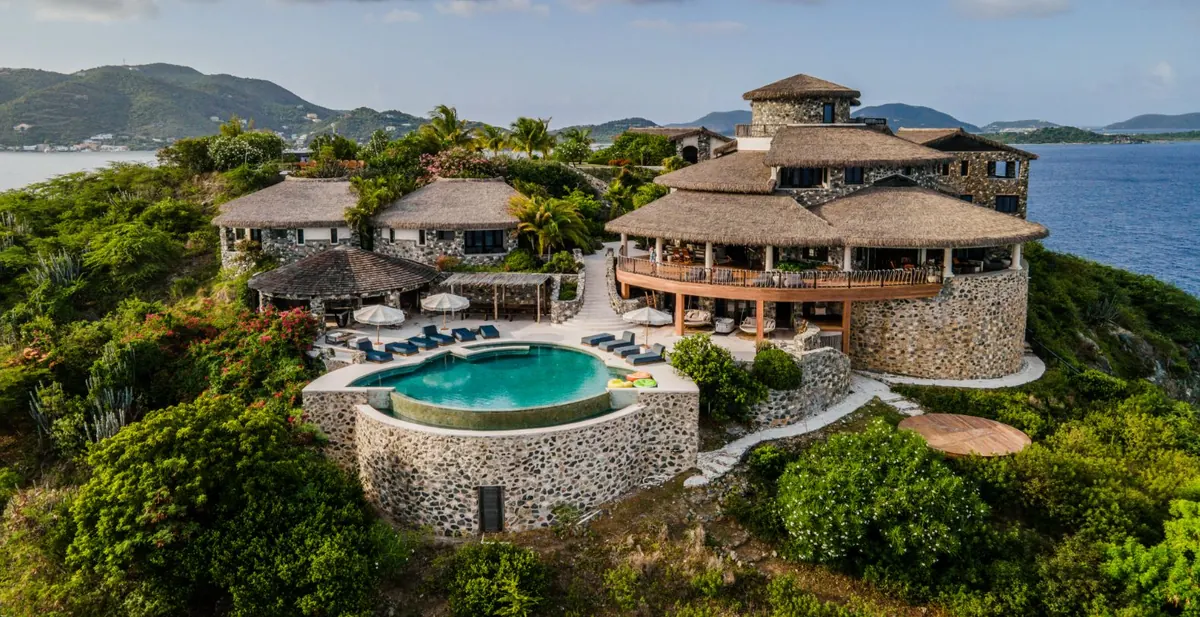 A stone island villa with thatched roofs and a swimming pool overlooking the sea