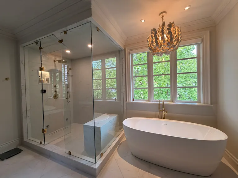 Finished primary bathroom with a marble-lined glass shower, a freestanding tub and brass fittings