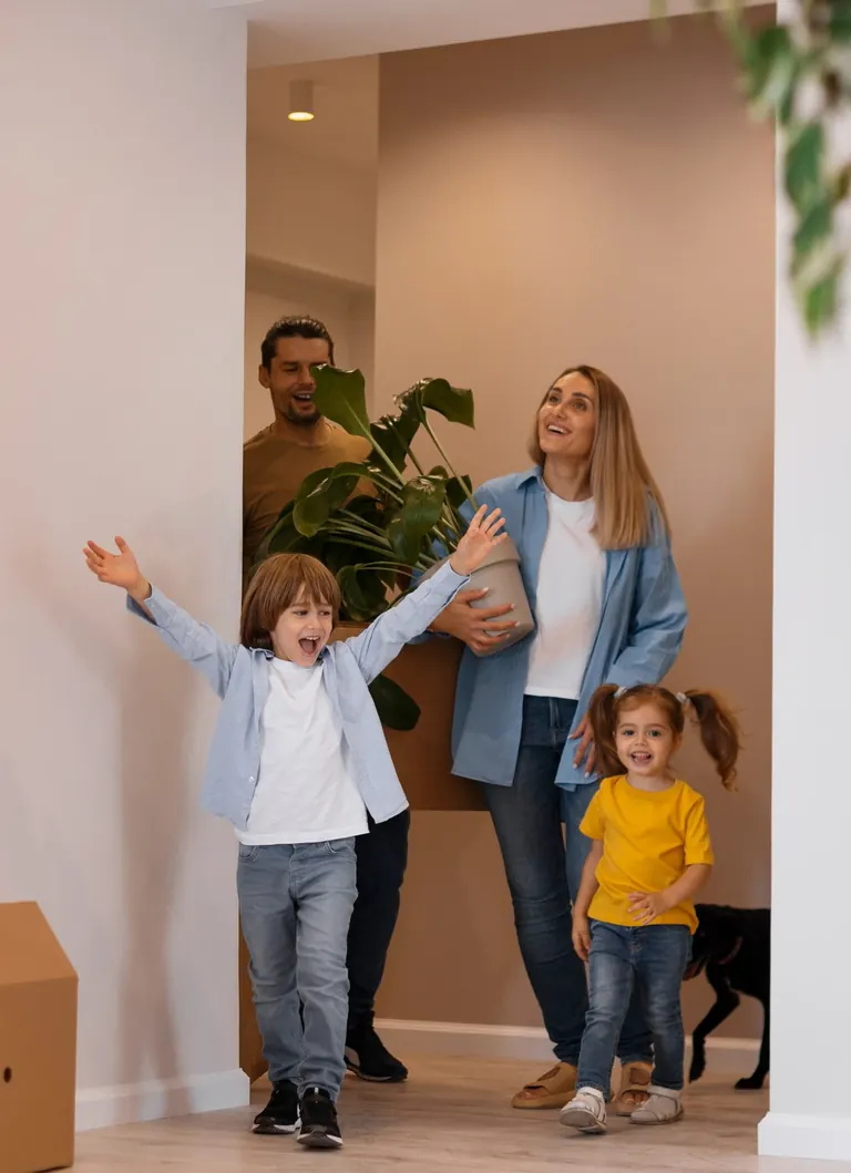 A family of four and their dog walking into the hallway of a newly finished home, with a moving box beside them
