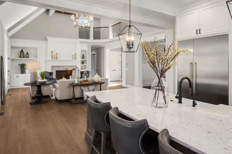 An open-plan kitchen island looking through to a double-height living room with a fireplace and a gallery landing above