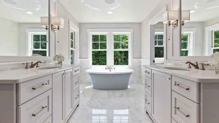 Finished primary bathroom with twin vanities, a freestanding tub and marble floors